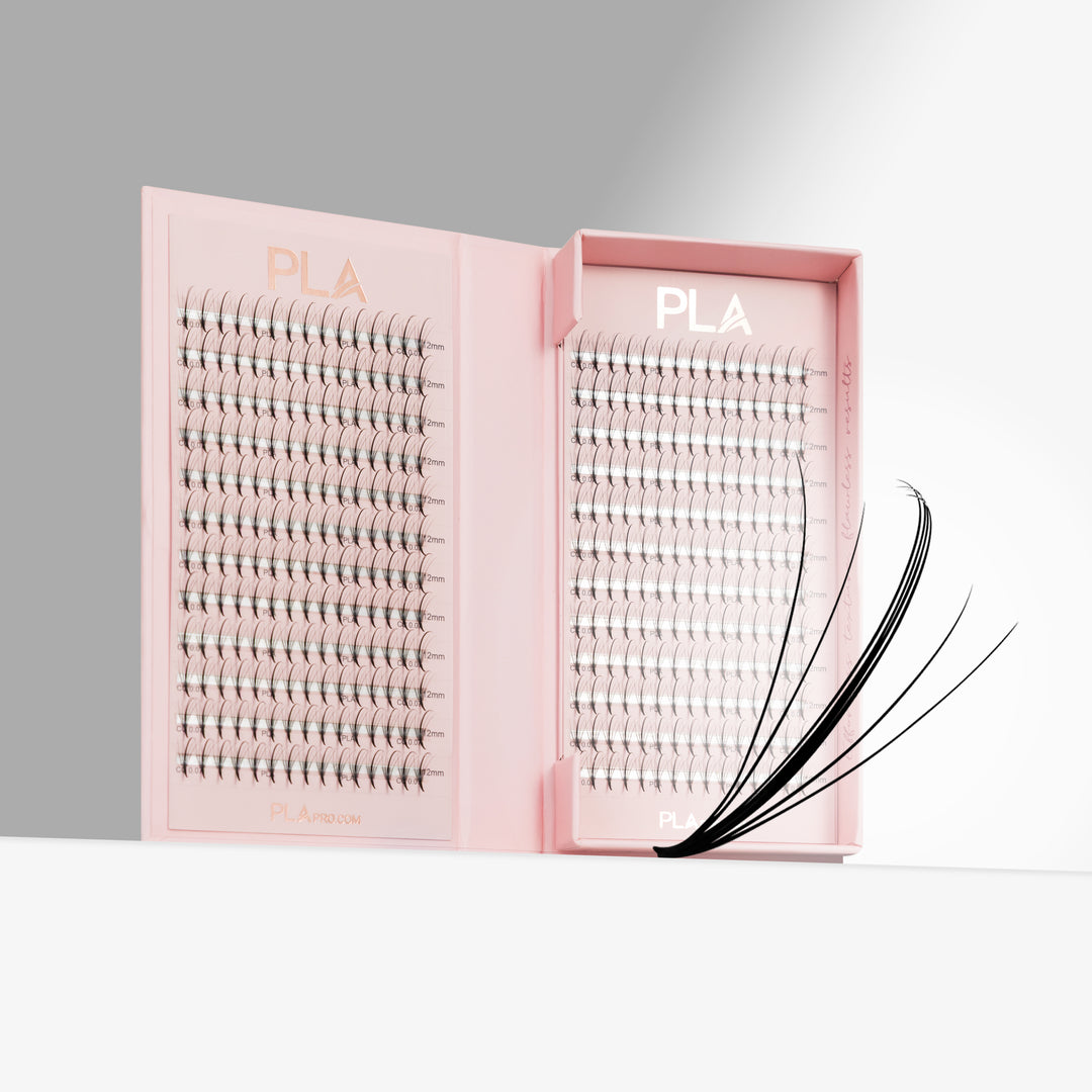 Pink tray of eyelash promades with an individual black promade fanned out in front, photographed on a clean white and gray studio background. The tray is labeled PLA.