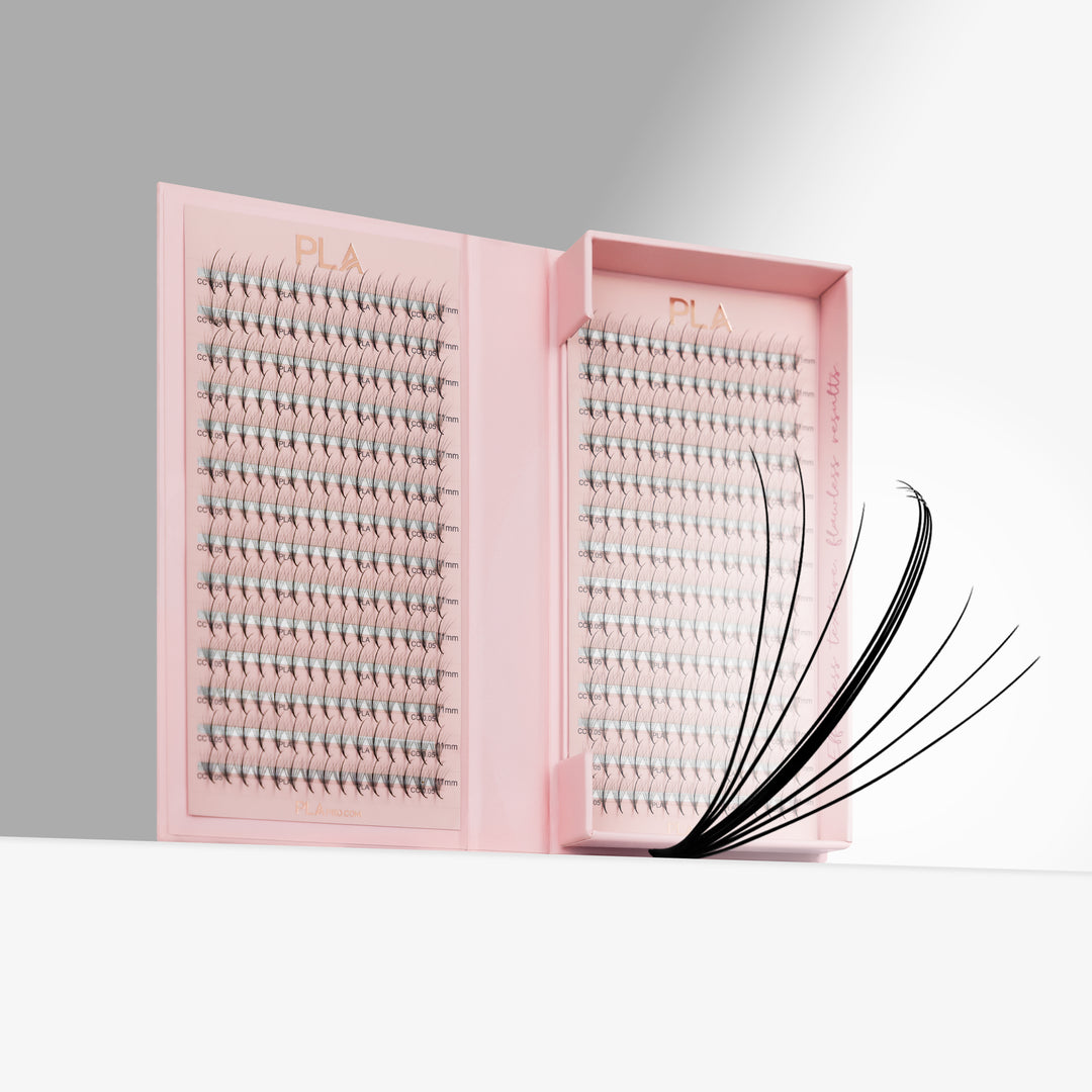 Pink lash tray packaging with rows of eyelash promades. Close up of wispy promade on the right side of open tray. All on a clean white and gray studio background.