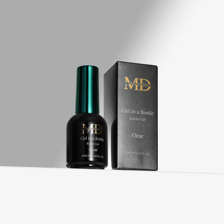 A bottle of MD Clear Gel In A Bottle nail gel stands next to its black packaging box with gold lettering on a clean white surface against a gray background.
