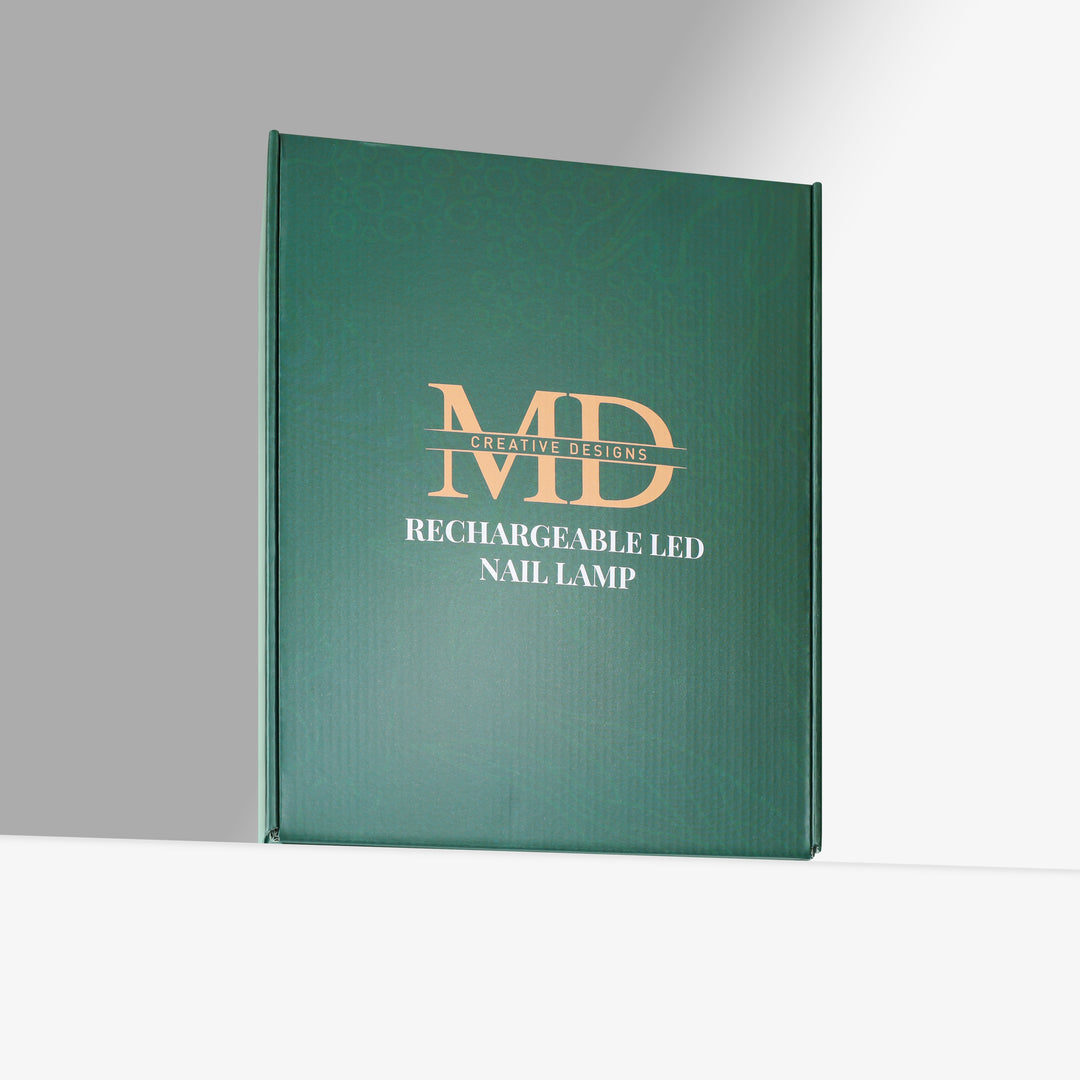 A dark green hardcover book or box standing upright on a white surface against a gray background. The front features gold and white text reading 'MD CREATIVE DESIGNS RECHARGEABLE LED NAIL LAMP'.