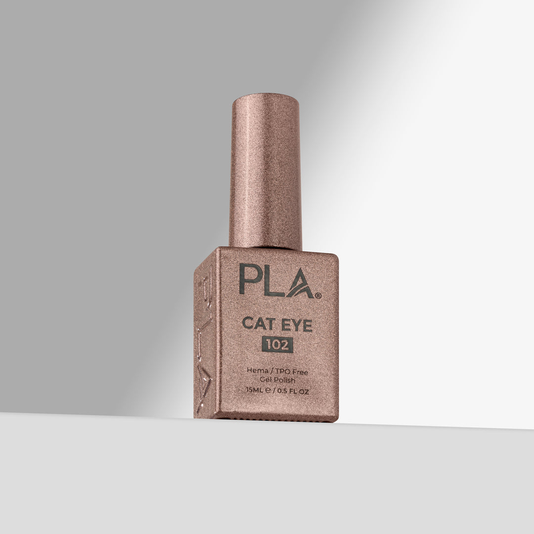 A bottle of PLA Cat Eye 102 nail polish in a shimmering rose gold color, standing on a light gray surface against a gray background 