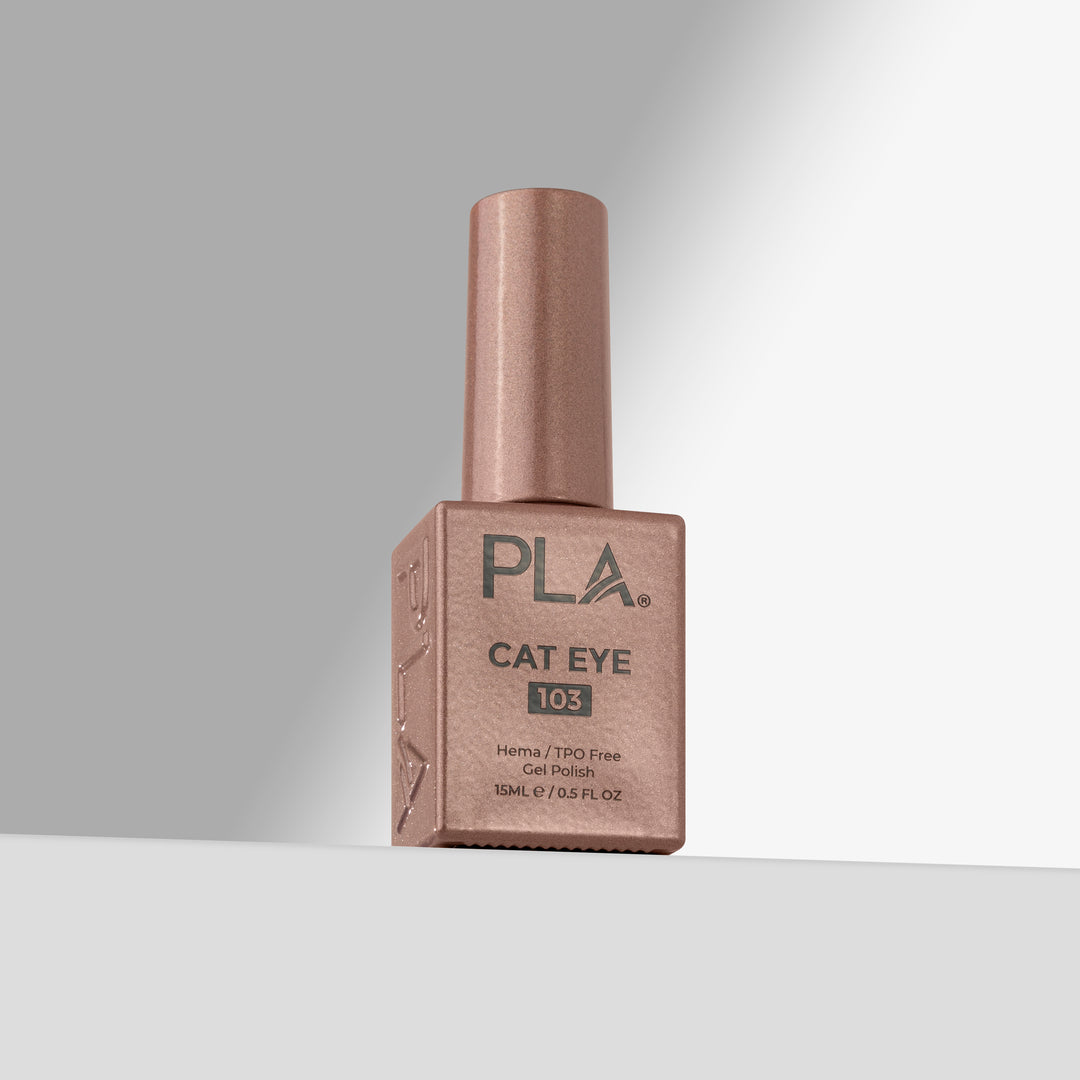 A bottle of PLA Cat Eye 103 gel nail polish in a rose gold shade, standing upright on a light gray surface against a gray background.