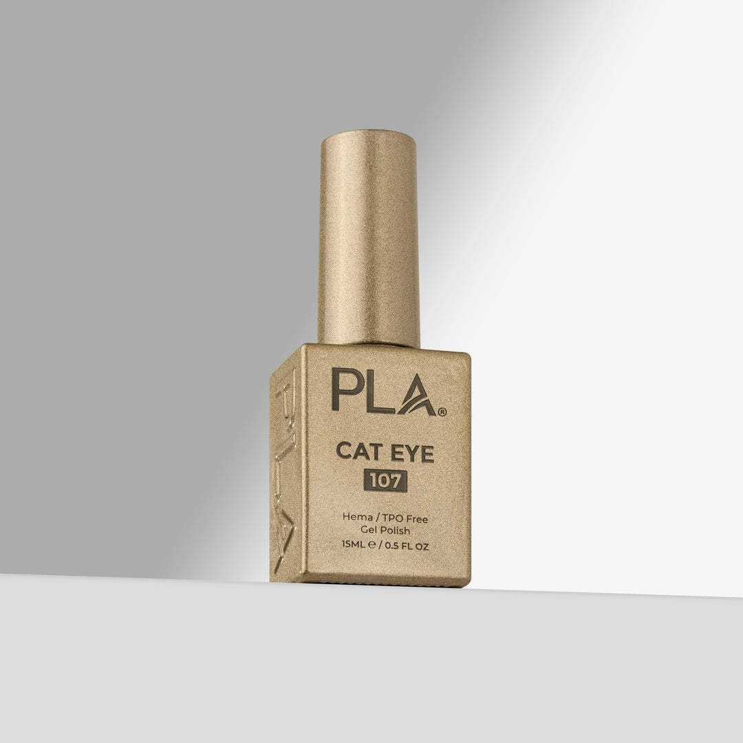 A bottle of PLA Cat Eye 107 gel nail polish in a gold color, standing upright on a light gray surface against a gray background.