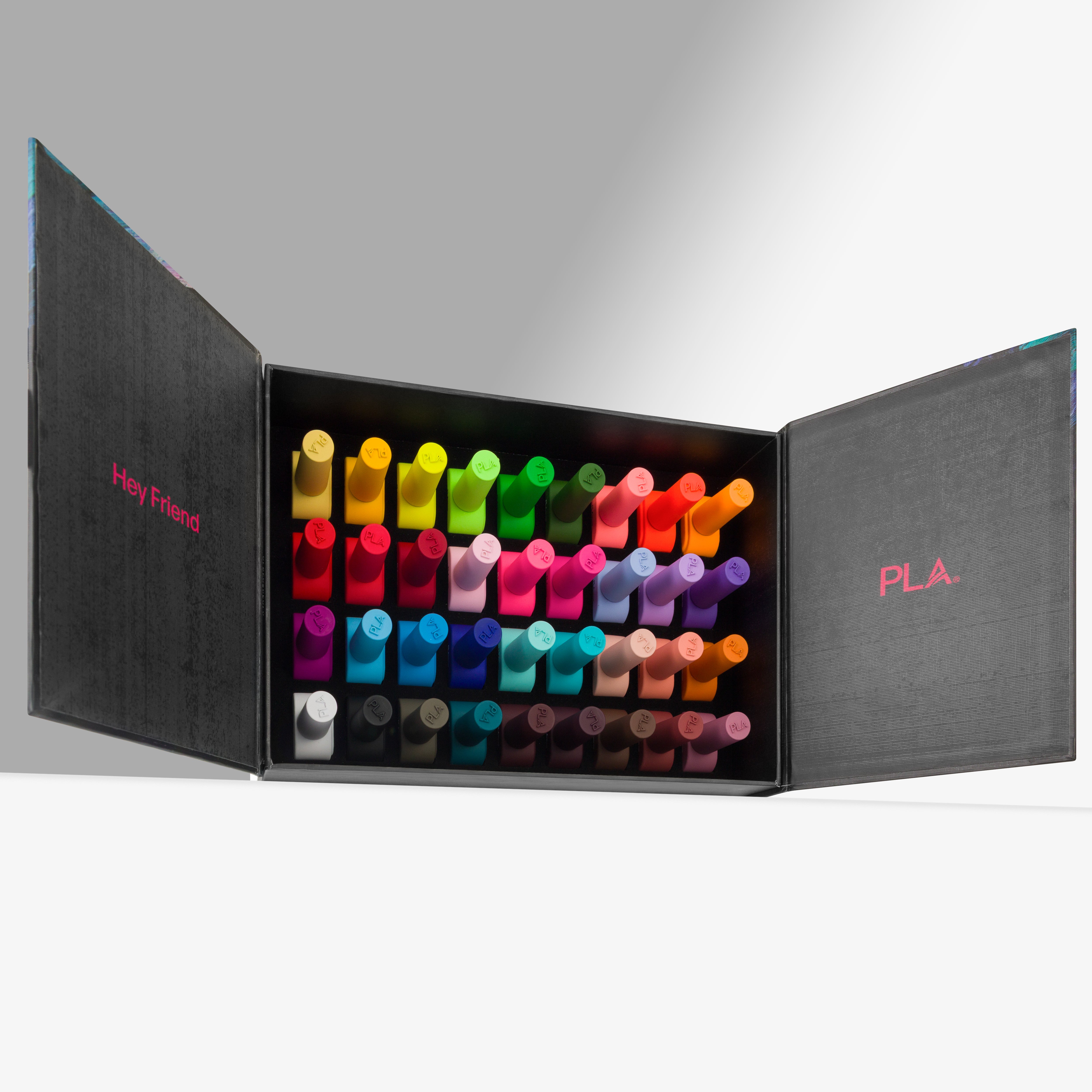 An open black presentation case displaying a set of colorful nail polish bottles arranged in rows. The left panel reads 'Hey Friend' in pink, and the right panel reads 'PLA.